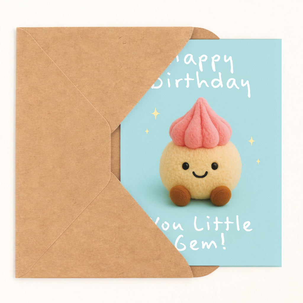 A cute birthday card with a kraft paper envelope, featuring a small smiling felt gem character with a pink frosting-like top on a light blue card with white text reading 'Happy Birthday' and 'You Little Gem!'.